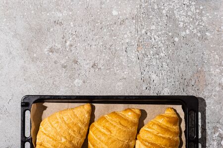 top view of baked delicious croissants on baking tray on concrete grey surfaceの写真素材