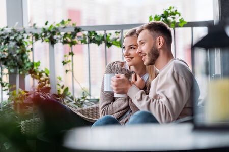selective focus of happy couple holding cups while sitting outsideの写真素材