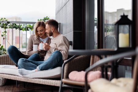 selective focus of happy woman and man holding cups while sitting on outdoor sofaの写真素材