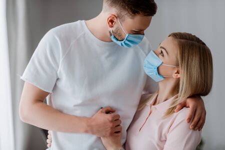 couple in medical masks holding hands and looking at each other