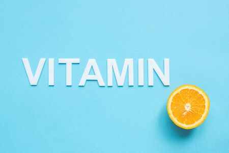 top view of ripe orange half and word vitamin on blue backgroundの写真素材
