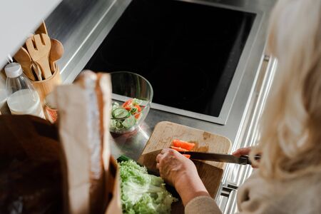 cropped view of elderly woman cutting vegetables on board for salad on kitchenの写真素材