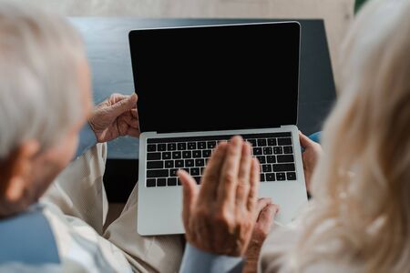 cropped view of senior couple waving and having video chat on laptop with blank screen at home during self isolationの写真素材