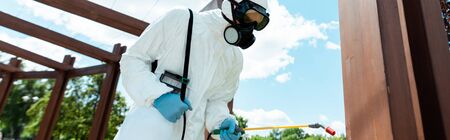 workman in hazmat suit and facemask disinfecting wooden construction in park during coronavirus pandemic, horizontal cropの写真素材