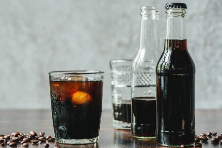 selective focus of cold brew coffee with ice in glass and bottles near coffee beansの写真素材