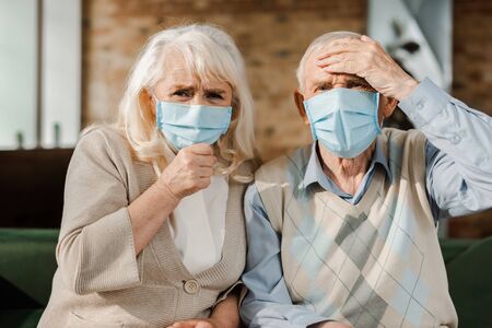 senior worried couple in medical masks sitting at home during self isolationの写真素材