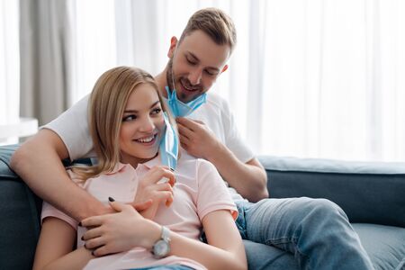 happy man and girl in medical masks smiling in living roomの写真素材