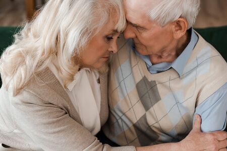 sad elderly couple hugging and sitting at home on quarantineの写真素材