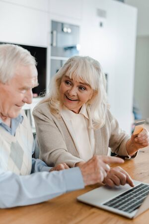 surprised elderly couple shopping online with credit card and laptop at home during quarantineの写真素材
