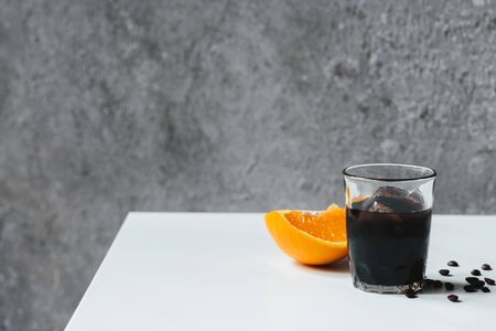 cold brew coffee with ice in glass near orange and coffee beans on white tableの写真素材