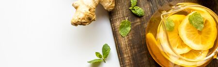 top view of hot tea with lemon near ginger root and mint on wooden cutting board on white background, panoramic shotの写真素材
