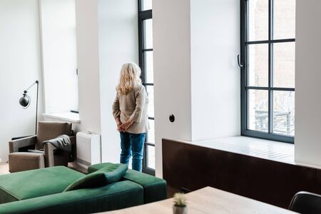 upset senior woman standing near window at home during quarantineの写真素材
