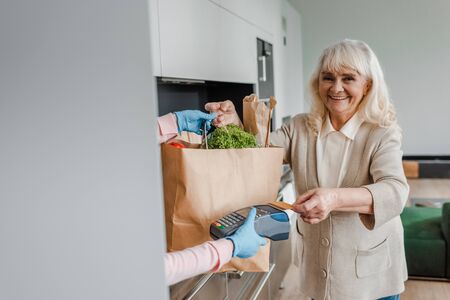 happy elderly woman taking food delivery and paying with credit card and terminal during coronavirus pandemicの写真素材