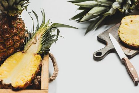 selective focus of fresh cut pineapple on wooden tray and cutting board with knife on white backgroundの写真素材