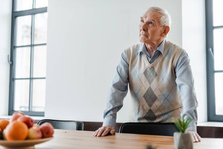 sad elderly man standing at table with fruits during quarantine, selective focusの写真素材