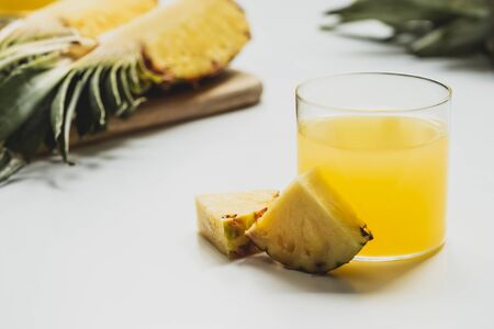 selective focus of fresh pineapple juice near cut delicious fruit on cutting board on white backgroundの写真素材