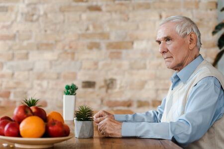 lonely senior man with fruits and plants on table during self isolation
