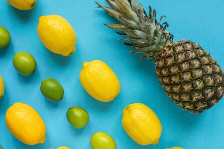 flat lay with ripe yellow lemons, green limes and pineapple on blue background
