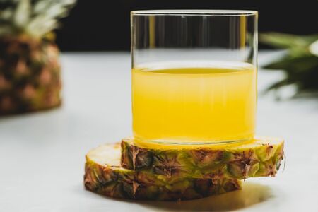 close up view of fresh pineapple juice on cut delicious slices on white backgroundの写真素材