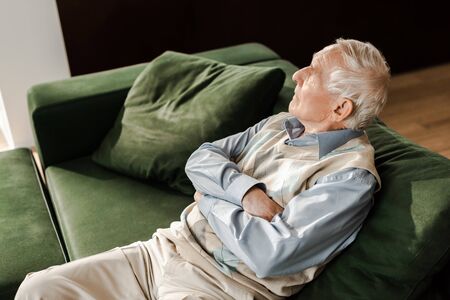 sad elderly man sitting with crossed arms on sofa during quarantineの写真素材