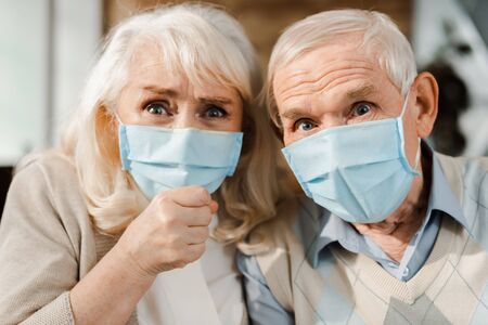 emotional elderly couple in medical masks showing fist during self isolation