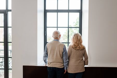 back view of upset elderly couple looking through window at home on quarantineの写真素材