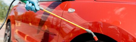 cropped view of specialist in uniform cleaning car with disinfectant in spray bag during covid-19...