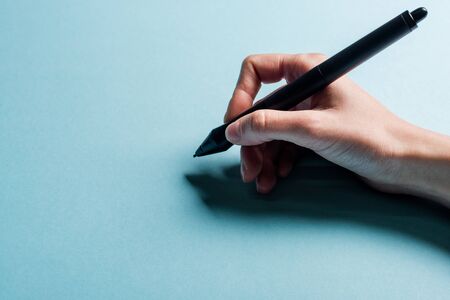 Cropped view of designer holding stylus of graphics tablet on blue background