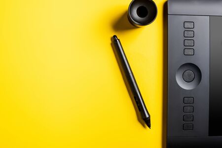 top view of black drawing tablet, stylus and holder on yellowの写真素材