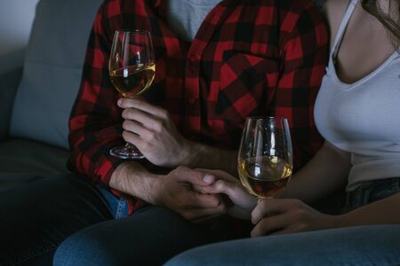 cropped view of couple holding hands while sitting on sofa with glasses of white wineの写真素材
