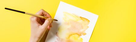 horizontal crop of artist holding paintbrush near painting on yellowの写真素材