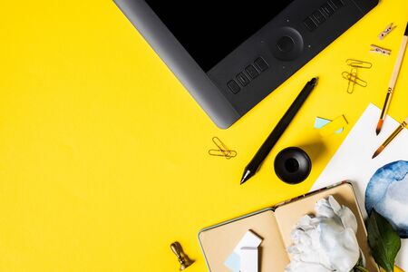 top view of painting, drawing tablet with blank screen, clips, stylus, notebook and flower on yellowの写真素材