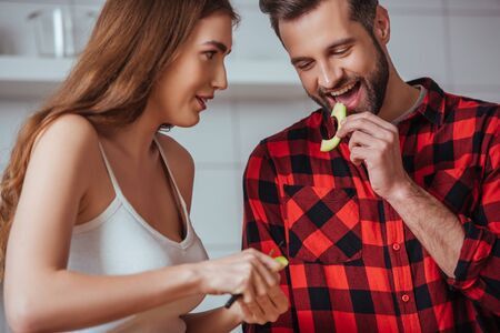 cheerful man tasting slice of fresh avocado near attractive girlfriendの写真素材