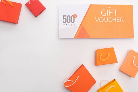 Top view of toy shopping bags near gift voucher with 500 dollar value lettering on white backgroundの写真素材