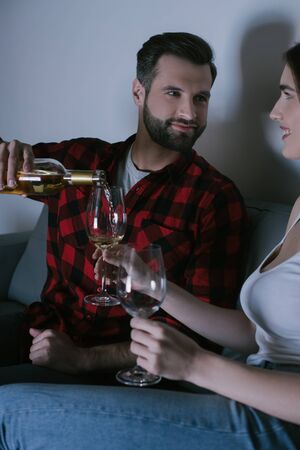 handsome man pouring white wine into glass near happy girlfriendの写真素材