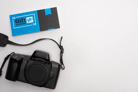 Top view of gift voucher near digital camera on white background with copy space