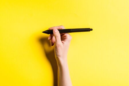 Cropped view of designer holding stylus of graphics tablet on yellow backgroundの写真素材