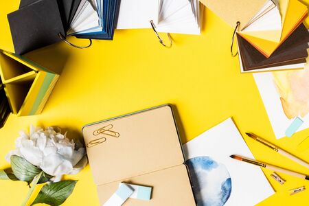 top view of paintbrushes, clips, paintings, blank notebook, flower and colorful palette on yellowの写真素材