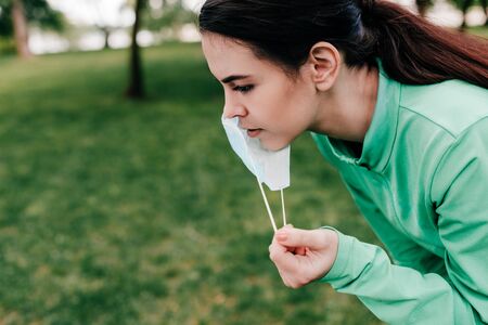 Side view of sportswoman taking off medical mask in park