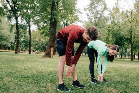 Young couple smiling while stretching together in parkの写真素材