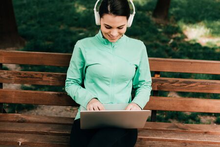 Beautiful smiling freelancer in headphones using laptop in parkの写真素材
