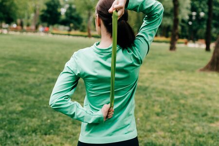 Back view of sportswoman pulling up resistance band in parkの写真素材
