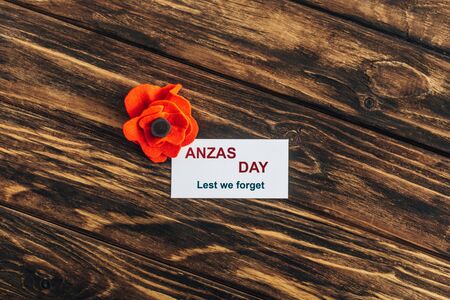 top view of artificial flower near card with anzas day lettering on wooden surface