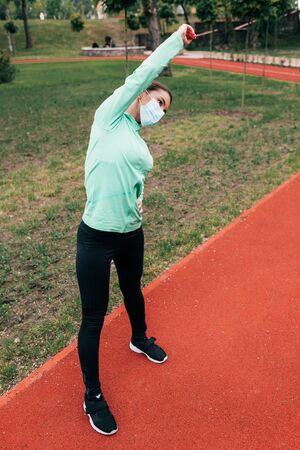 Young woman in medical mask working out on running track in parkの写真素材