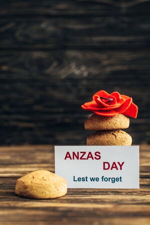 card with anzas day lettering near artificial flower and tasty cookies on wooden surfaceの写真素材