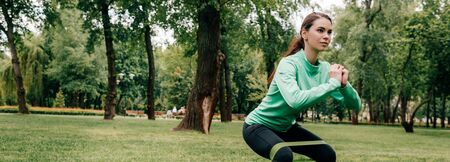 Panoramic crop of sportswoman doing squat with resistance band in park