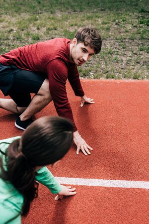 Overhead view of man looking at girlfriend while standing in starting position on running track in...