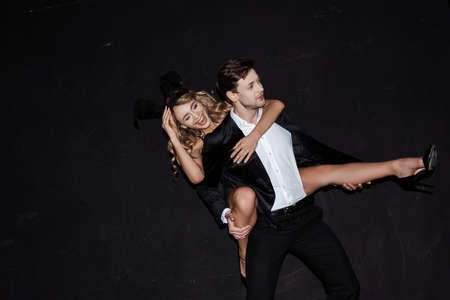 Attractive girl in bunny ears laughing while piggybacking on man in suit isolated on black