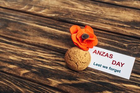 card with anzas day lettering near artificial flower and cookie on wooden surfaceの写真素材
