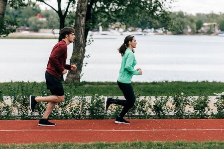 Side view of couple running on running track in parkの写真素材
